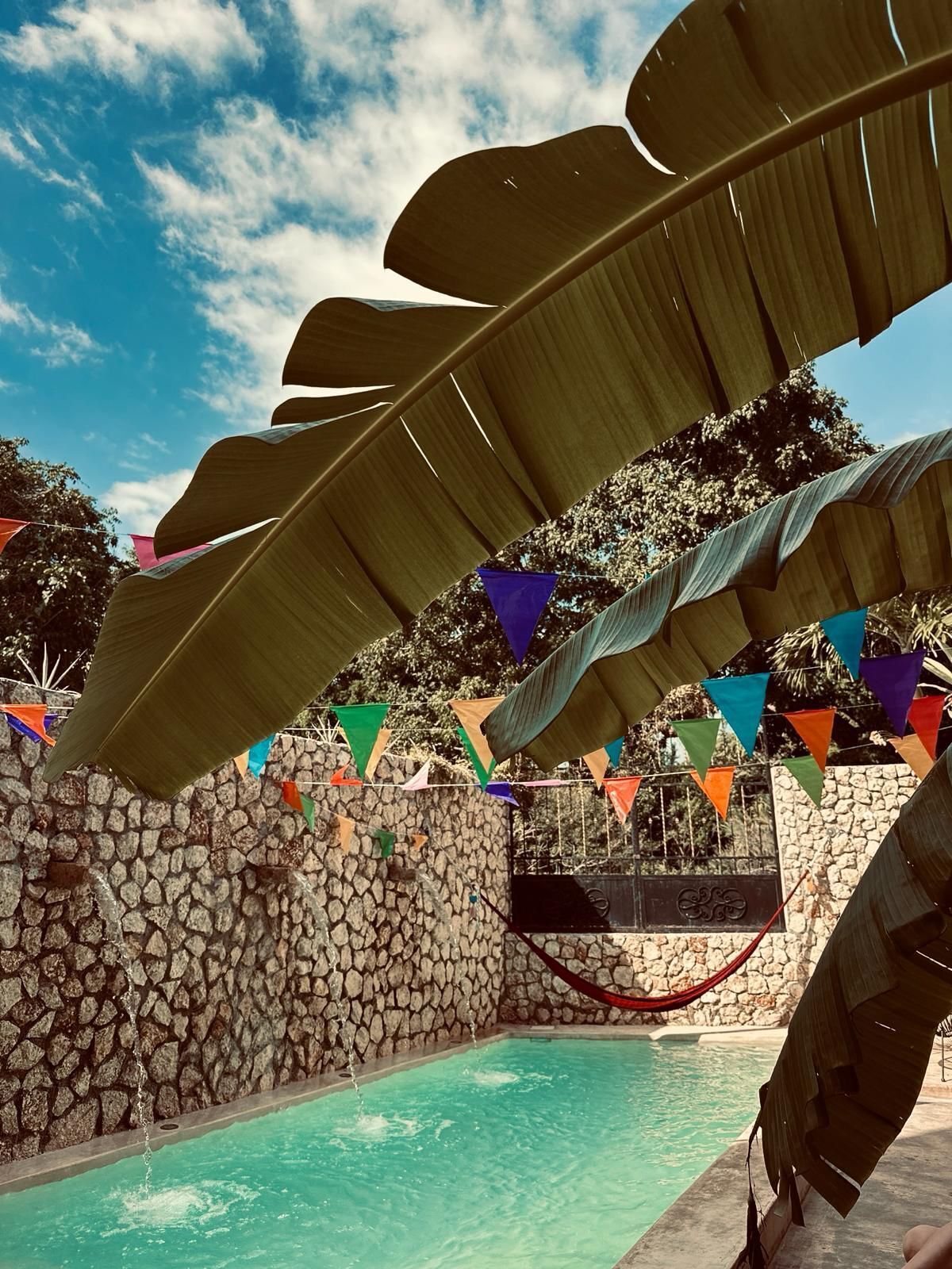 Un área de piscina con un muro de piedra, una hamaca y banderas triangulares de colores.