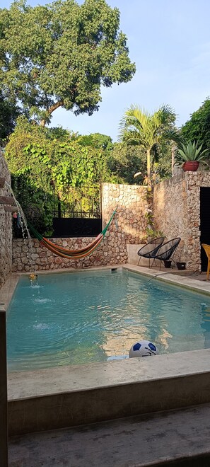 Una piscina con un muro de piedra, una hamaca y dos sillas.