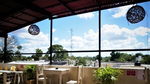 An outdoor seating area with tables and chairs, potted plants, and a view of the cityscape through large windows. - HOSTEL VALLADOLID 48 (Valladolid)