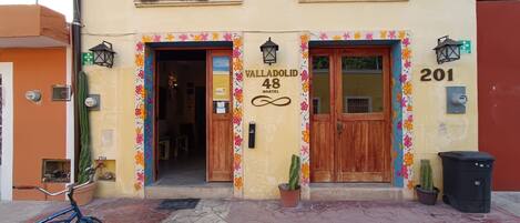 A hostel with a colorful floral border, wooden doors, and a sign reading "Valldolid 48 Hostel".