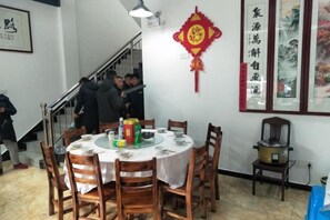 A dining area with round tables and chairs, a staircase, and traditional wall decorations. - Yiyuanchun Shanju Hotel (Huangshan City)