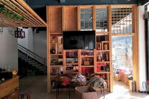 A room with a wooden bookshelf, a flat-screen TV, a staircase, and a view through a large window.