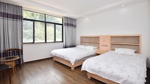 Habitación de hotel con dos camas, piso de madera, ventana con cortinas, una mesa con sillas y una lámpara en el techo.