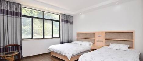 Habitación de hotel con dos camas, piso de madera, ventana con cortinas, una mesa con sillas y una lámpara en el techo.