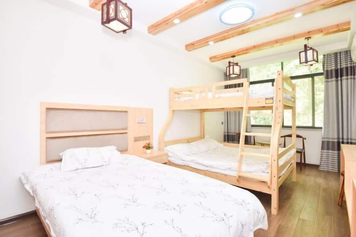 A room with bunk beds, a wooden headboard, a small table, and a window with curtains.