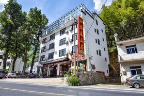 A multi-story hotel with a traditional architectural style, featuring a prominent entrance with a red awning and a visible restaurant or cafe area. - Yiyuanchun Shanju Hotel (Huangshan City)