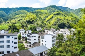 A cluster of white buildings with flat roofs, surrounded by lush green hills. - Yiyuanchun Shanju Hotel (Huangshan City)