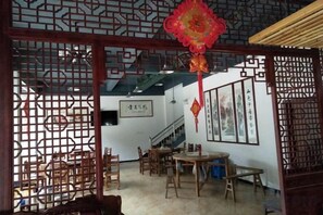 A traditional interior with a wooden table and chairs, a staircase, and decorative screens. - Yiyuanchun Shanju Hotel (Huangshan City)