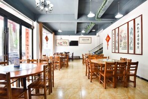 A restaurant interior with wooden tables and chairs, a staircase, and framed artwork on the walls. - Yiyuanchun Shanju Hotel (Huangshan City)