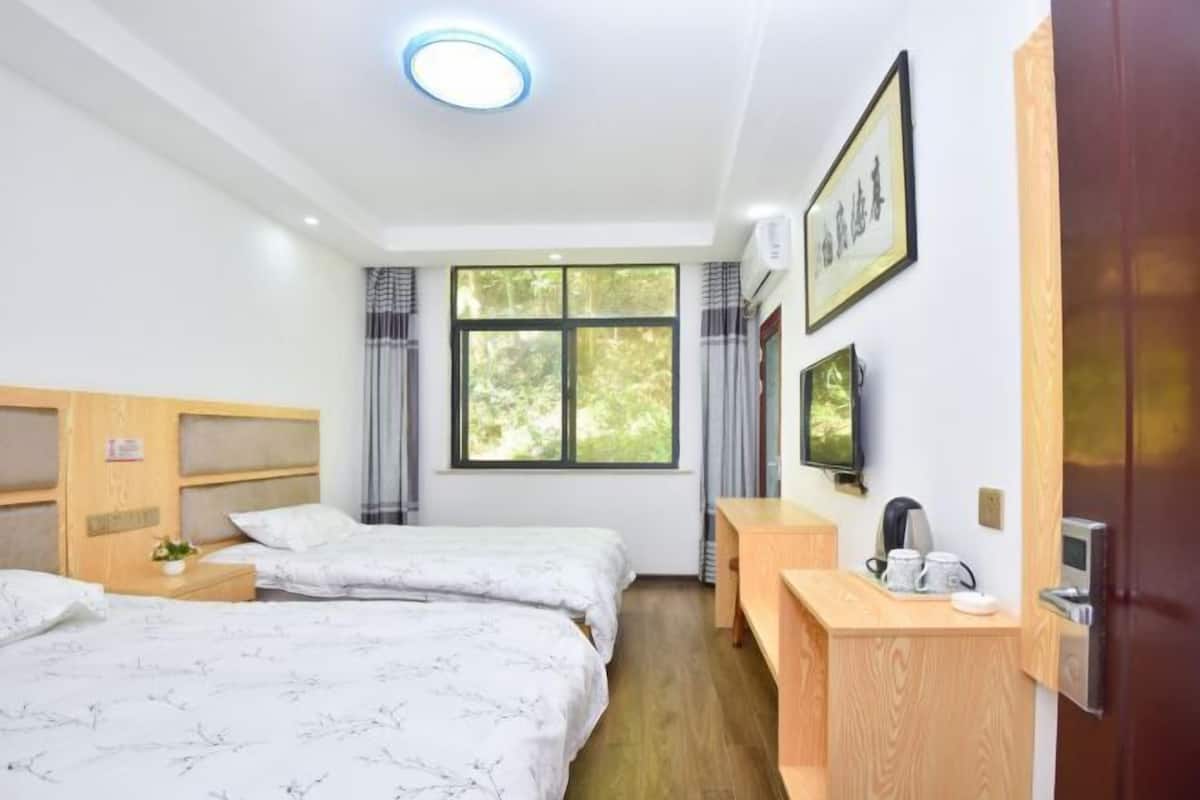 A hotel room with two beds, a wooden desk, a television, and a window with curtains.