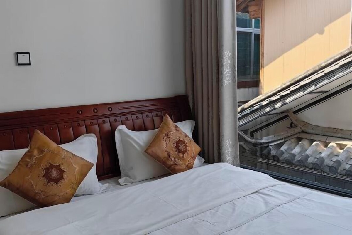 A hotel room with a wooden headboard, two decorative pillows, and a view of a staircase outside.