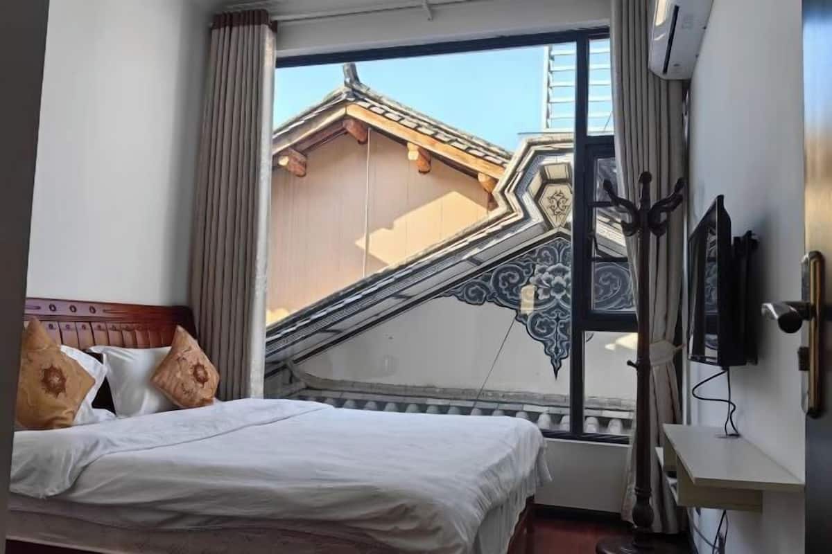 Une chambre d’hôtel avec un lit, une fenêtre donnant sur la façade d’un immeuble et un téléviseur fixé au mur.