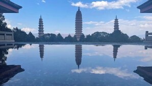 A serene reflection of pagodas in a calm water body, surrounded by trees and clear skies. - Hmyway (Dali City)