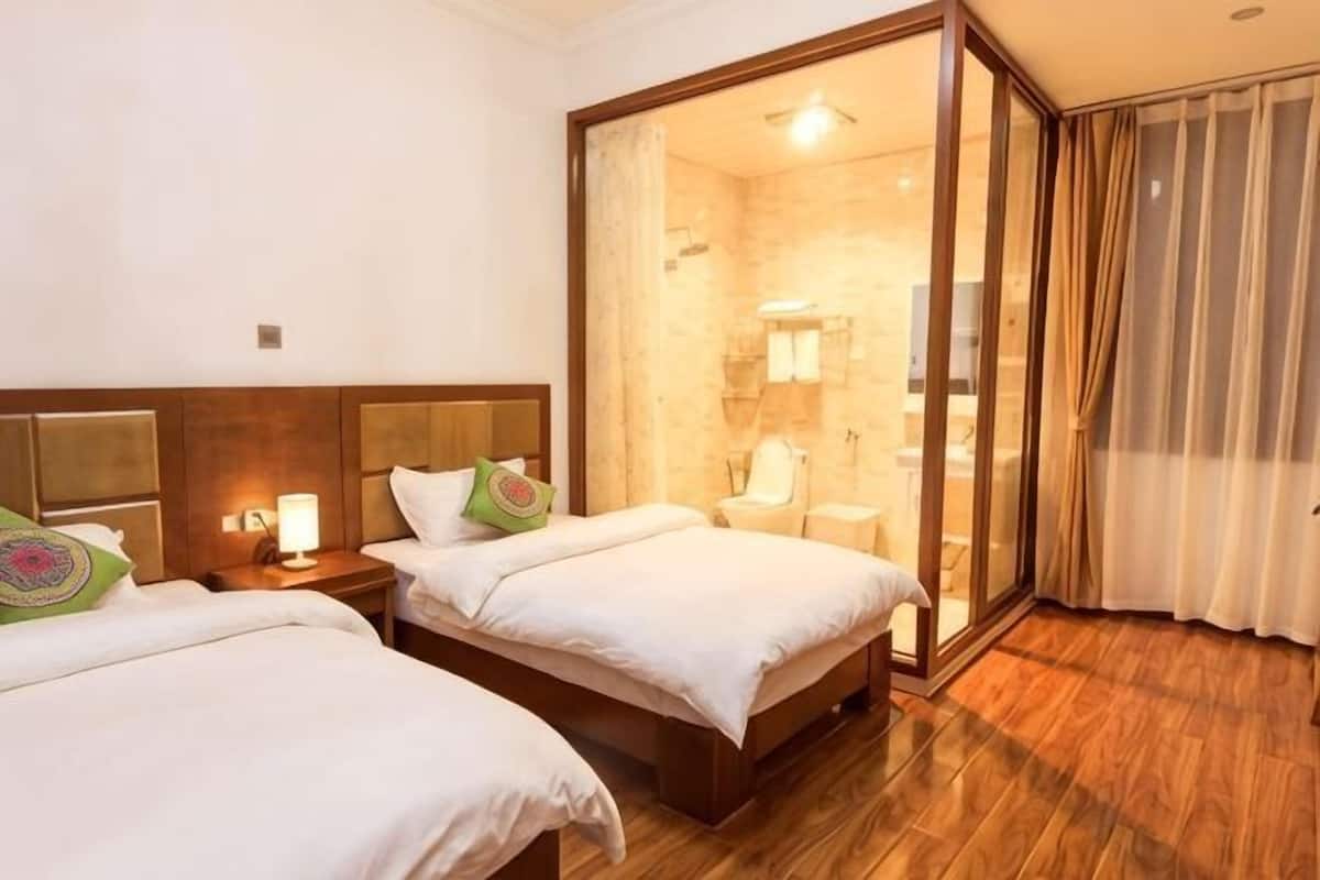 Une chambre d’hôtel avec deux lits, une tête de lit en bois, une porte en verre donnant sur une salle de bain et un plancher en bois.