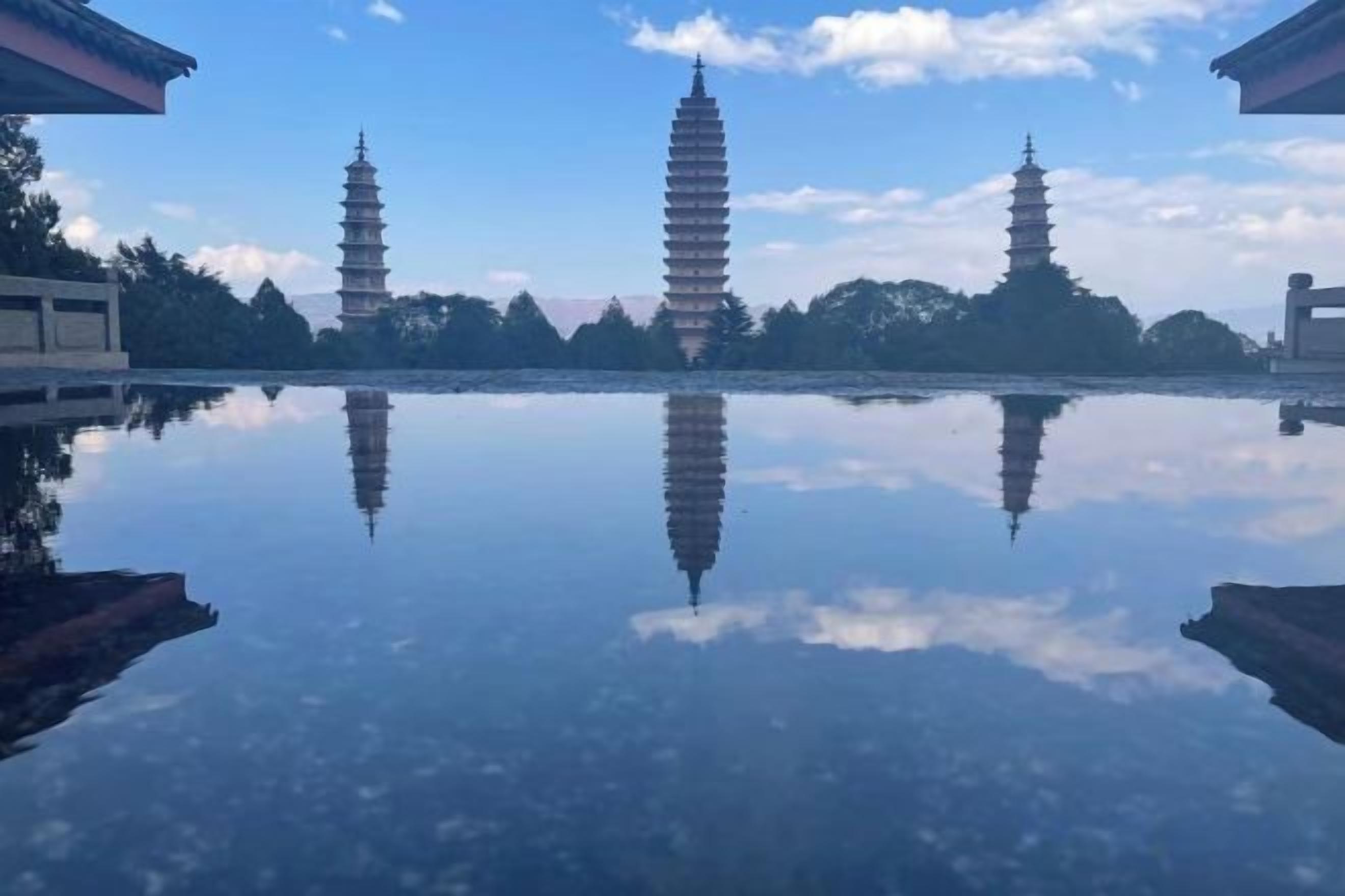 A reflection of pagodas on a calm water surface, surrounded by trees and buildings. - Hmyway (Dali City)