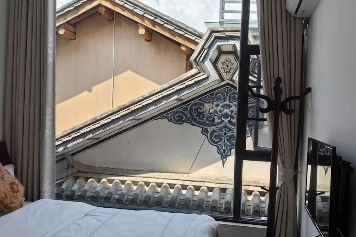 Une chambre avec un lit, une fenêtre donnant sur un immeuble et un garde-corps en métal décoratif.