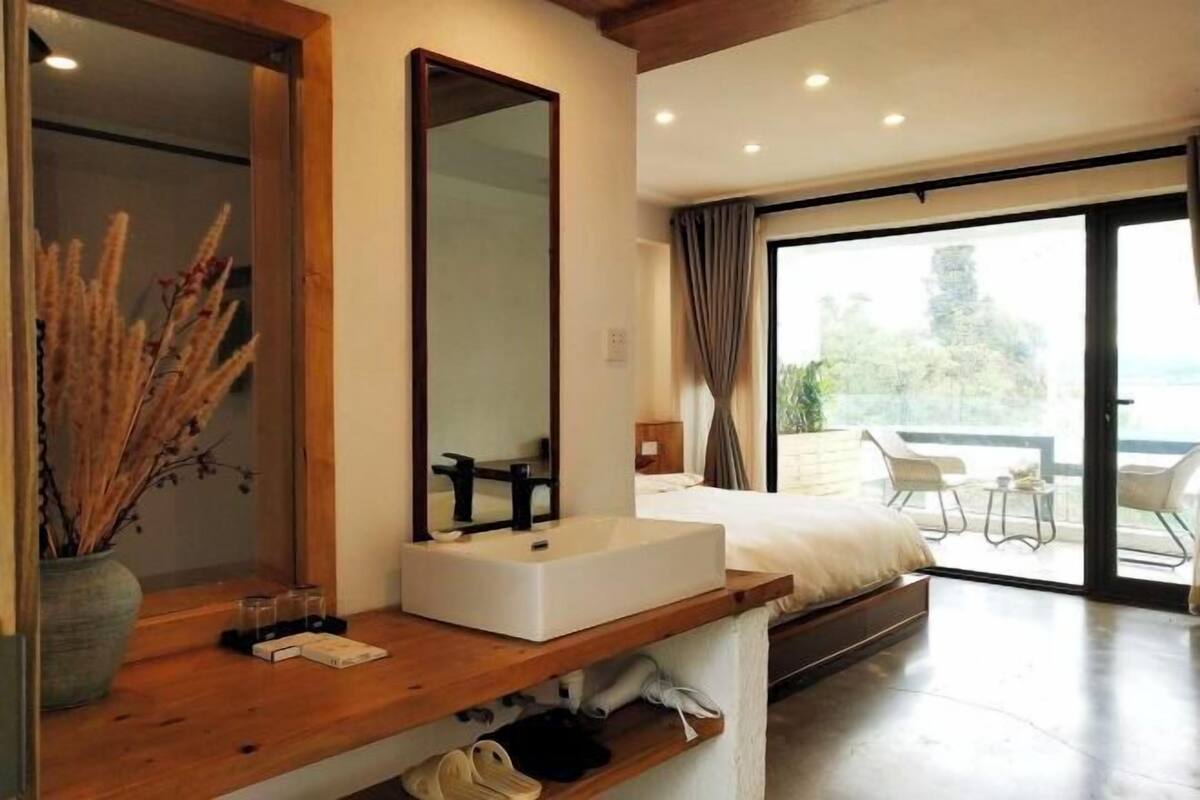 Une chambre moderne avec une grande fenêtre, une table de chevet avec un miroir, un lavabo blanc et un lit.