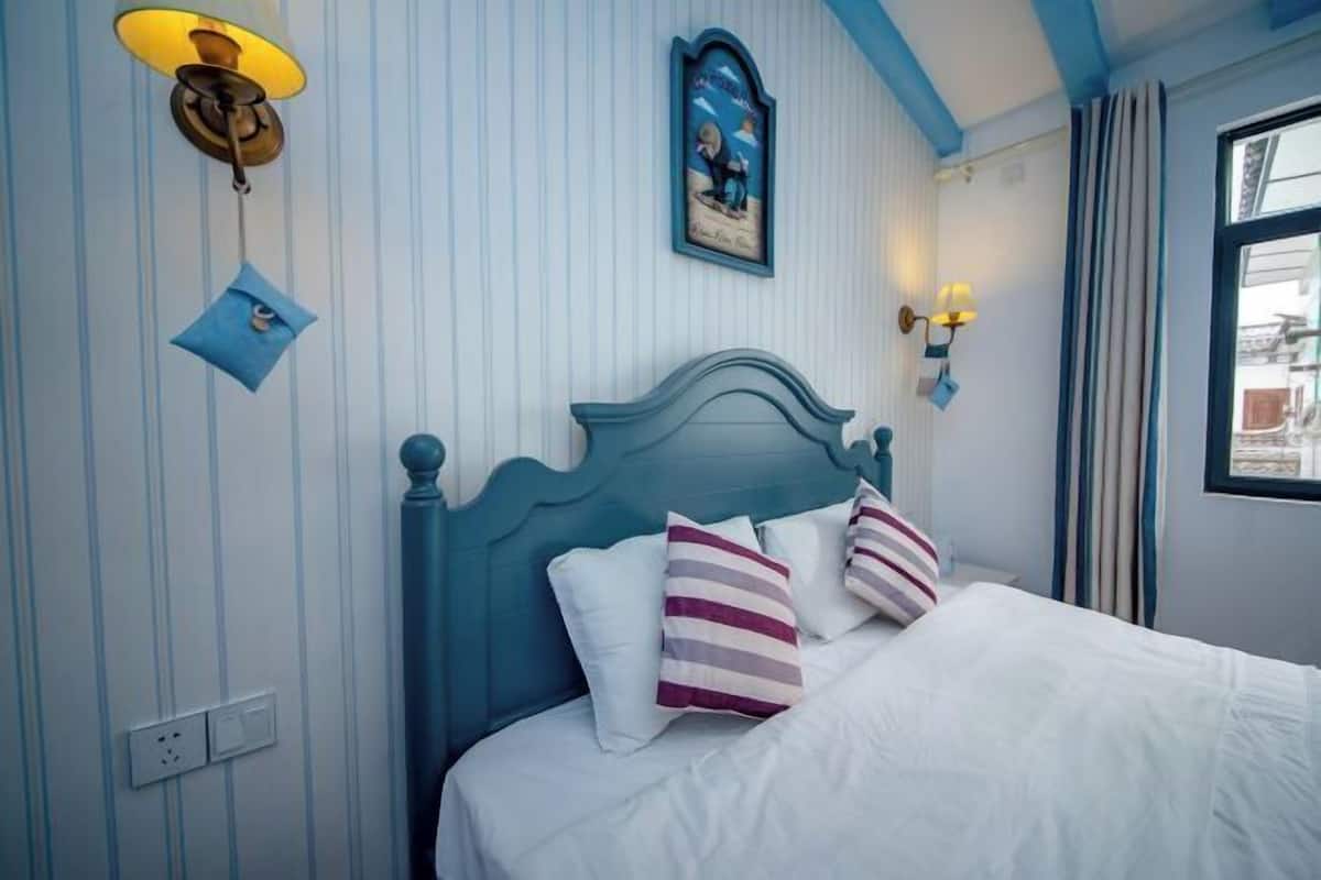 Une chambre à coucher avec un lit, des coussins à rayures, une lampe fixée au mur et un tableau encadré.