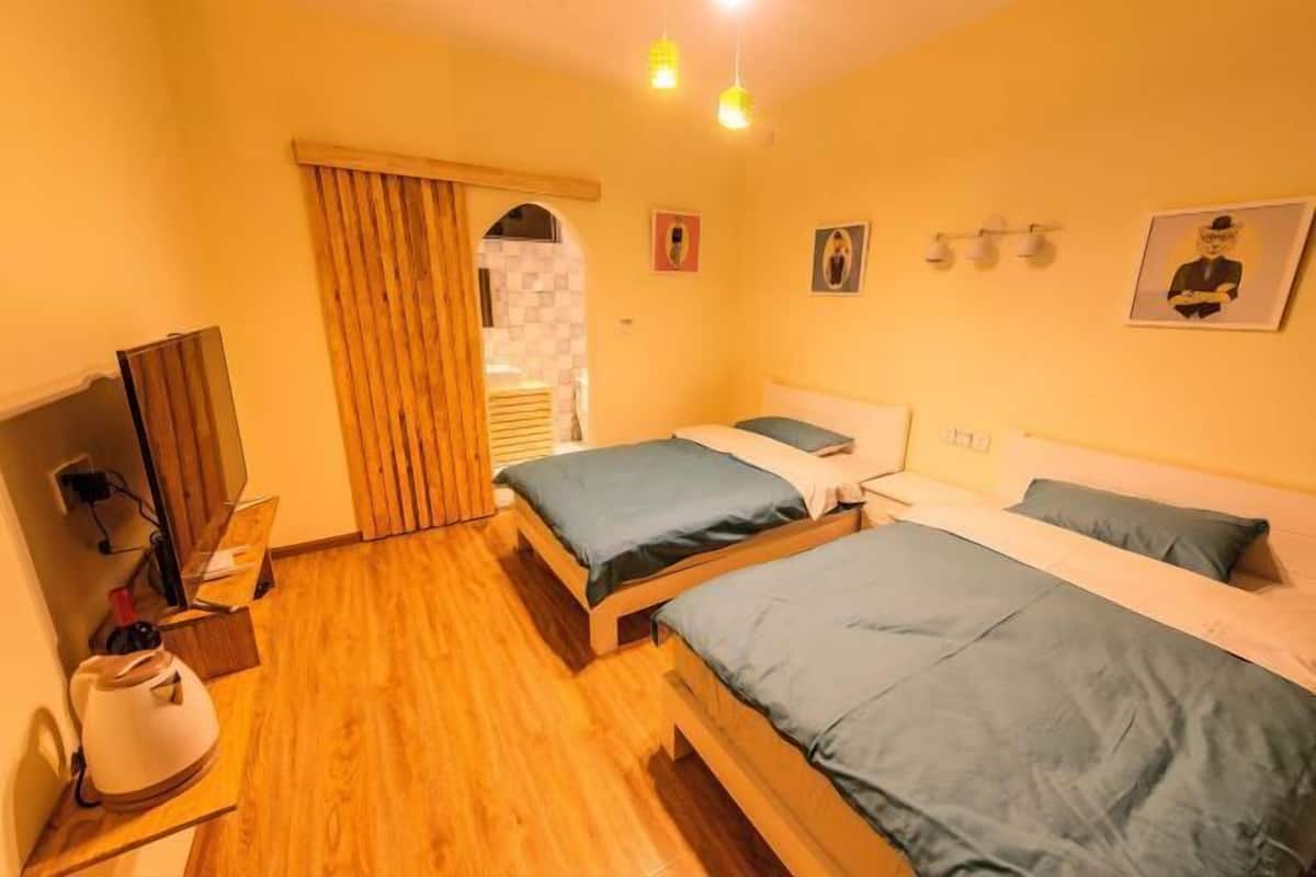 Une chambre avec deux lits, un plancher en bois, un bureau avec une lampe et une télévision.