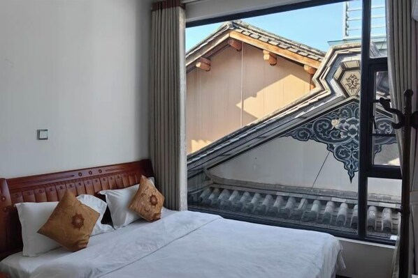 A hotel room with a bed, a window with a view of traditional architecture, and a curtain.