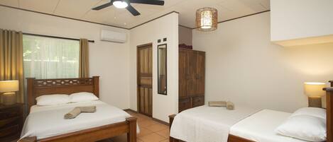 A hotel room with two wooden beds, a ceiling fan, a window with curtains, a wardrobe, and a bedside lamp.