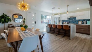 Eine moderne Küche mit Kochinsel, Pendelleuchten und einem Essbereich mit Holztisch und Stühlen.