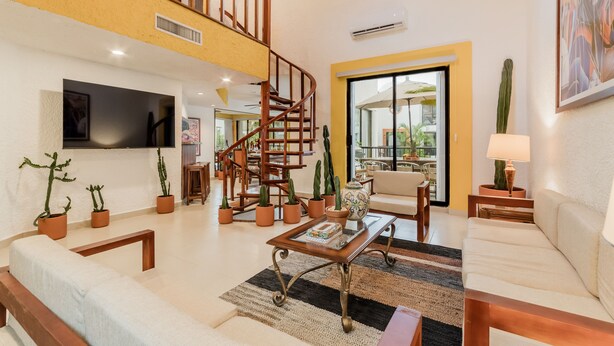A spacious living room with a wooden staircase, a flat-screen TV, multiple potted plants, and a comfortable seating area. - Zoque's Mexican Villa (Cancún)
