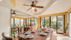A dining area with a long wooden table set for a meal, large windows, and a ceiling fan. - Zoque's Mexican Villa (Cancún)