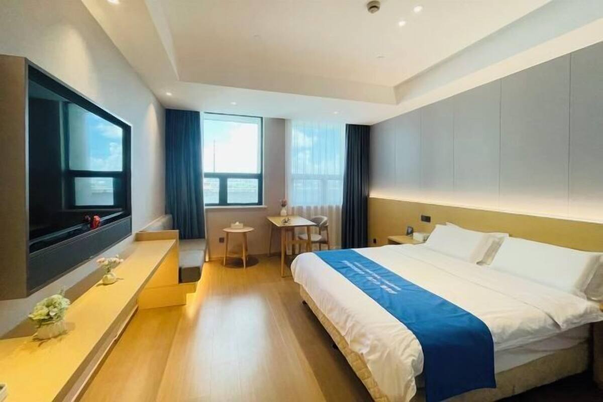 A hotel room with a bed, a TV mounted on the wall, a small table with chairs, and a window with curtains.