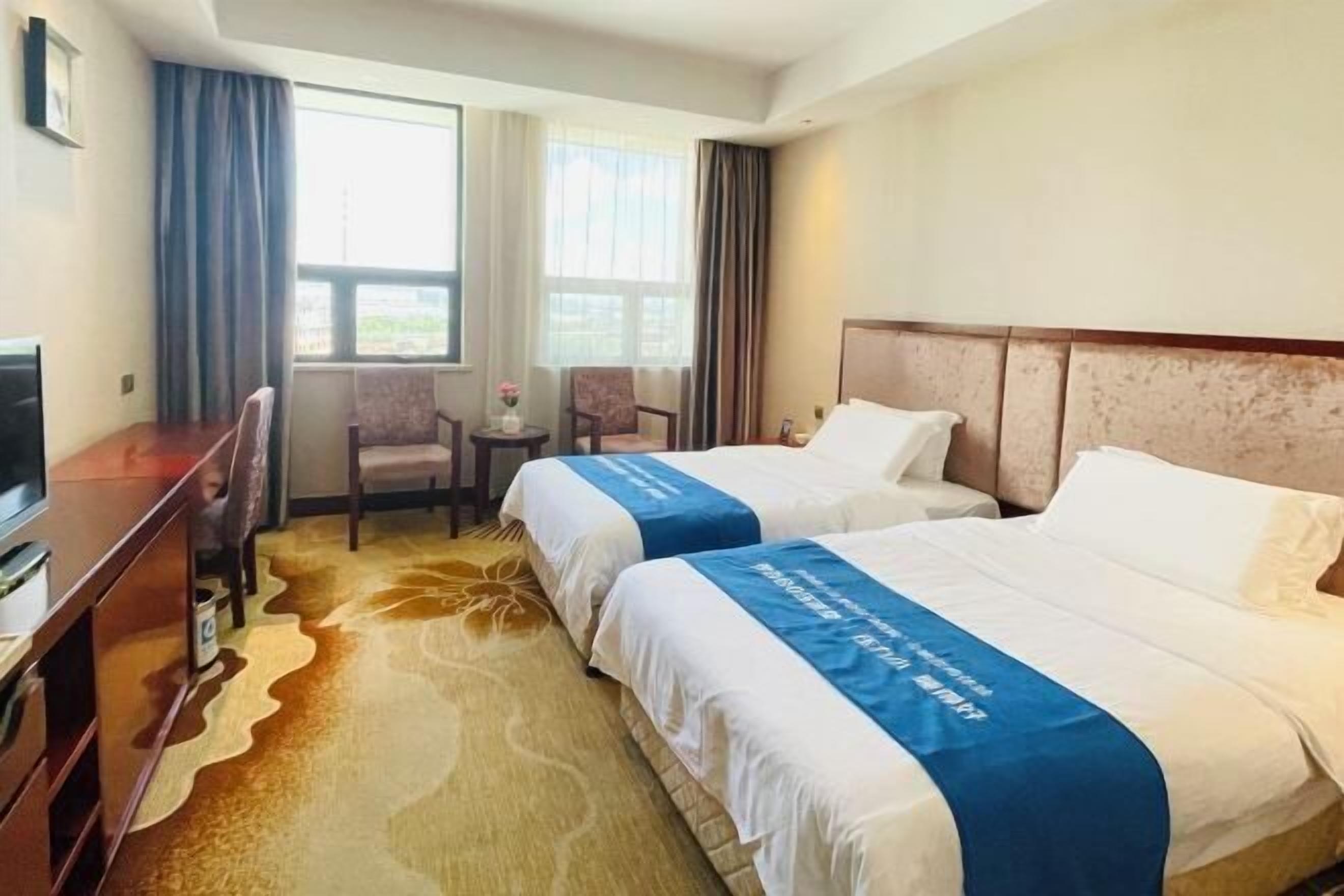 A hotel room with two beds, a TV, a small table, and a window with curtains.