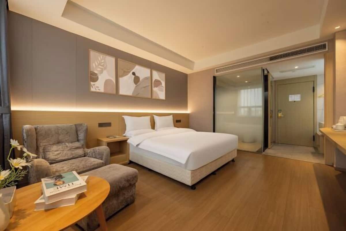 A hotel room with a bed, a sofa, a table with a book, and artwork on the wall.