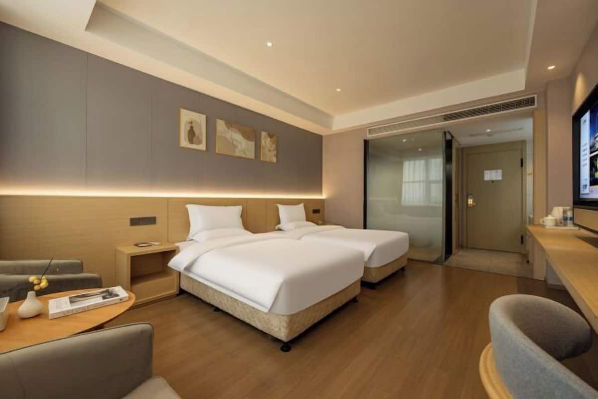 A hotel room with two beds, a desk, a chair, a TV, and artwork on the wall.