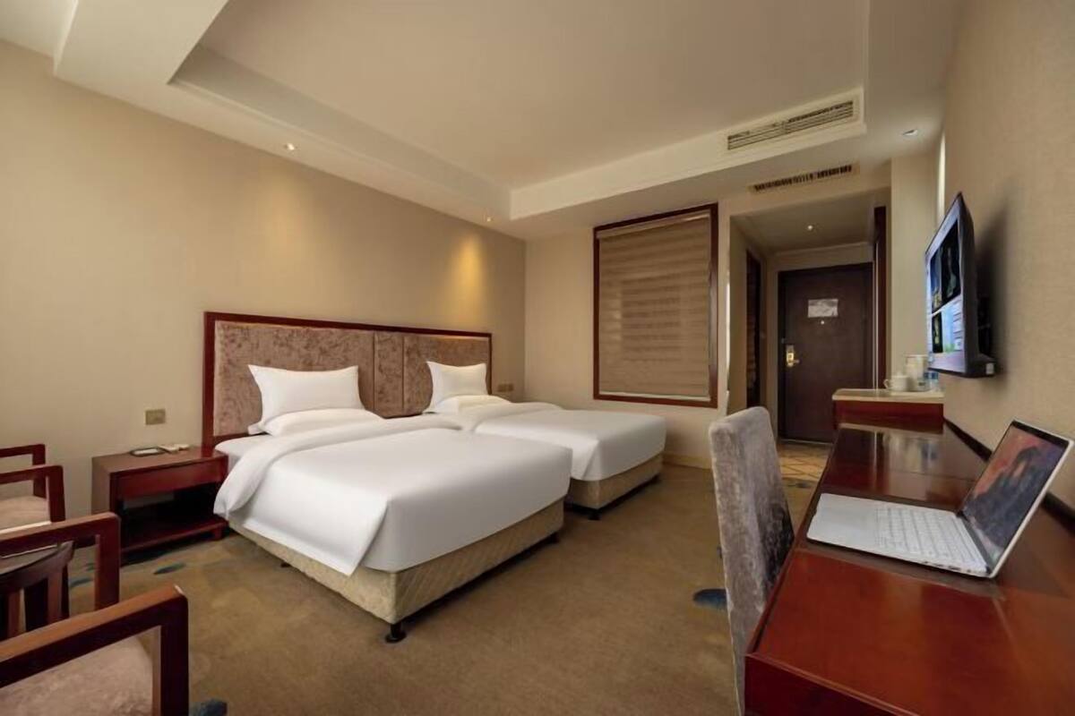 A hotel room with two beds, a desk with a laptop, a TV, and a door leading to another room.