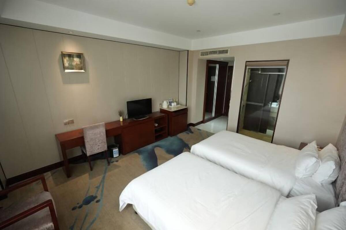 A hotel room with a bed, a desk with a TV, a mirror, and a wardrobe.
