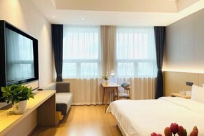 Habitación de hotel con cama, escritorio, computadora, silla, televisor y una planta.