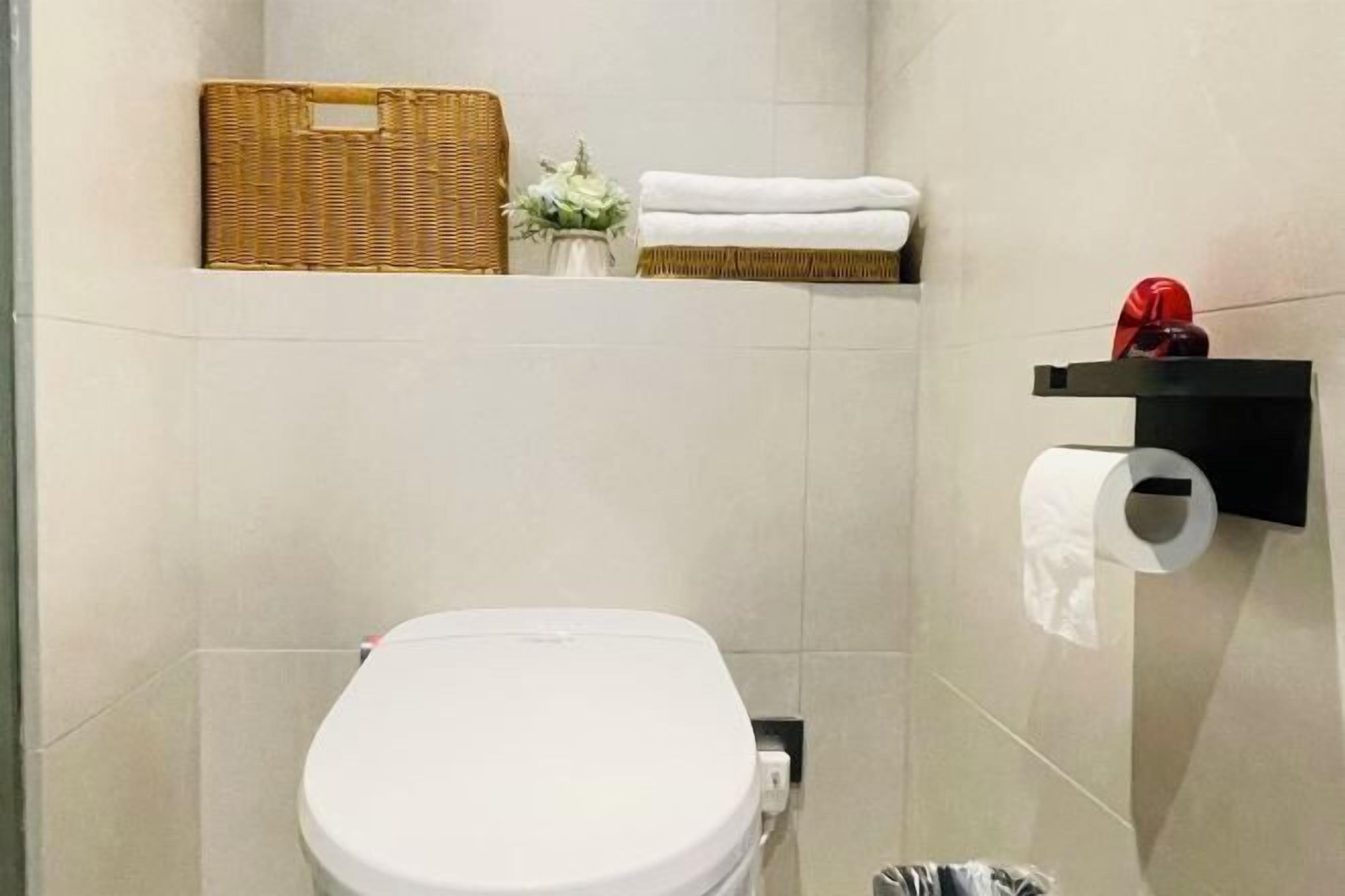 Une salle de bain avec des toilettes, un panier, un vase avec des fleurs et un porte-serviettes.