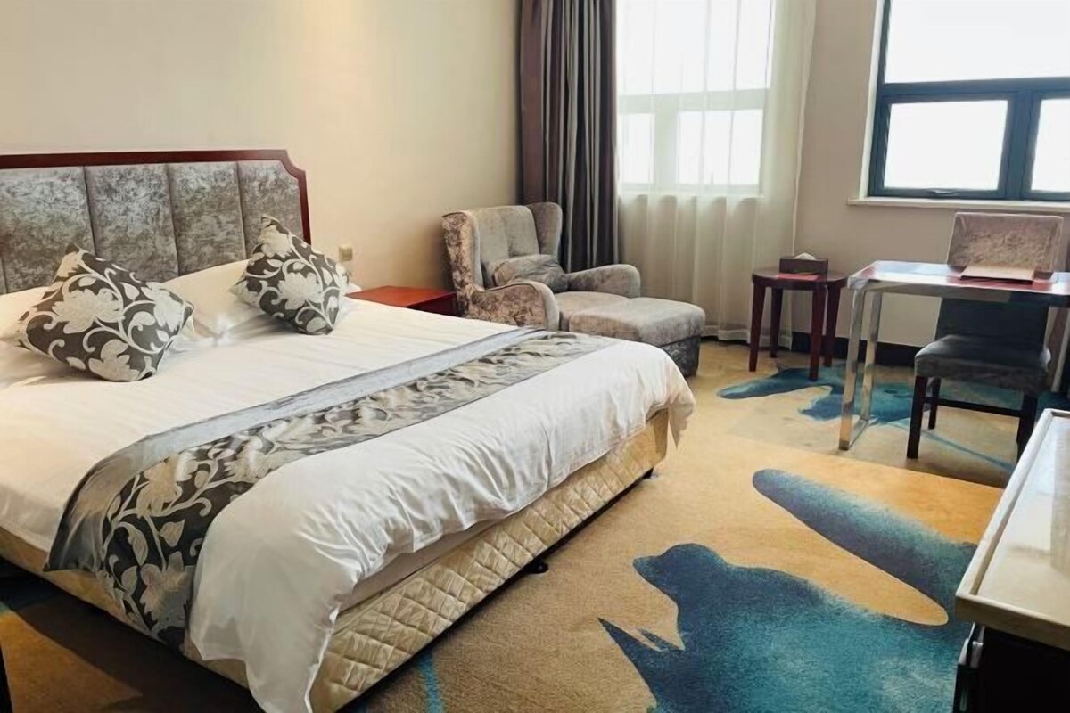 Habitación de hotel con una cama grande, una silla, un escritorio y vistas al exterior a través de una ventana.