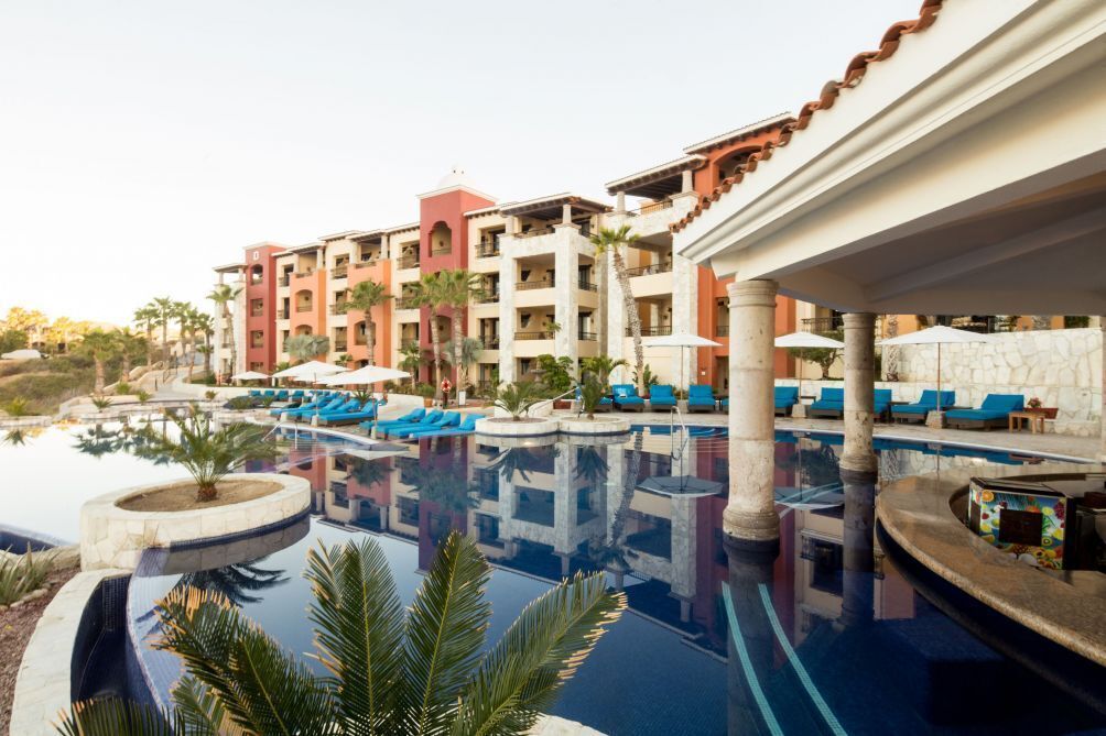 A resort with a central swimming pool, multiple balconies, and palm trees.