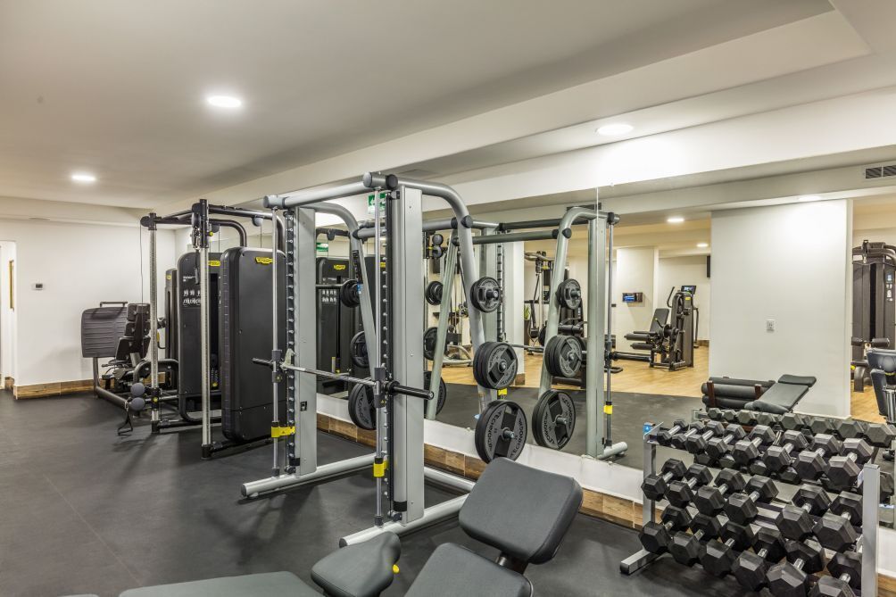 Un gimnasio con equipo de levantamiento de pesas, bancos y mancuernas.