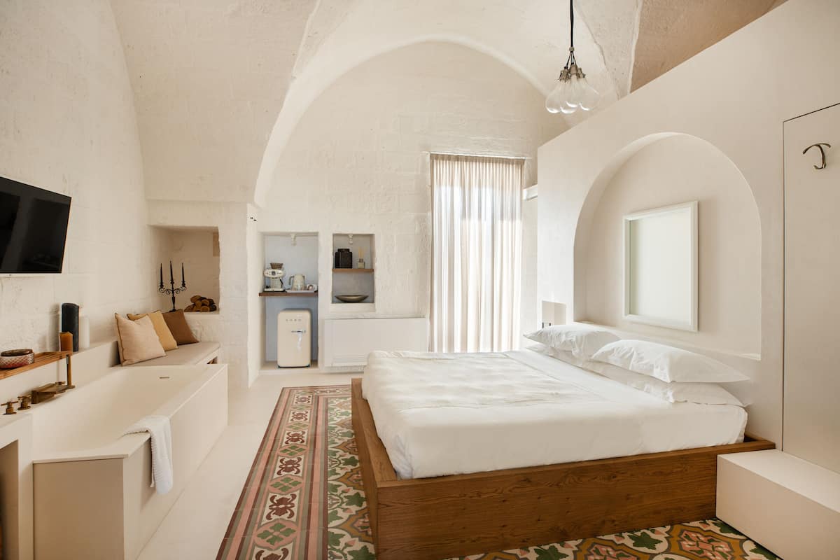 A bedroom with a wooden bed, a built-in TV, a small kitchenette, and a large window with curtains.