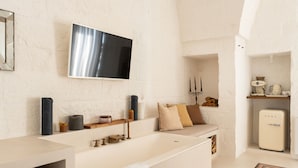 Un baño moderno con una bañera grande, un televisor montado y un refrigerador pequeño.