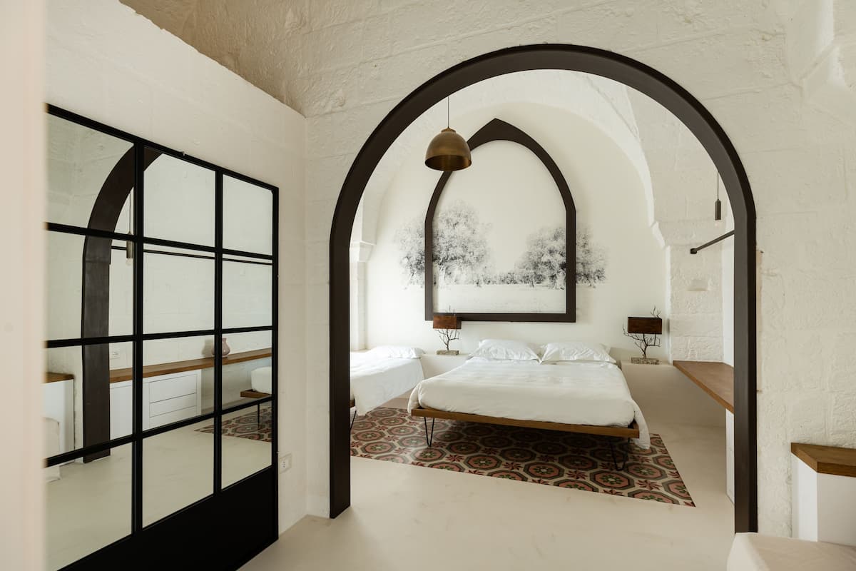 A bedroom with a large bed, a mirror, and a view of trees through an arched window.