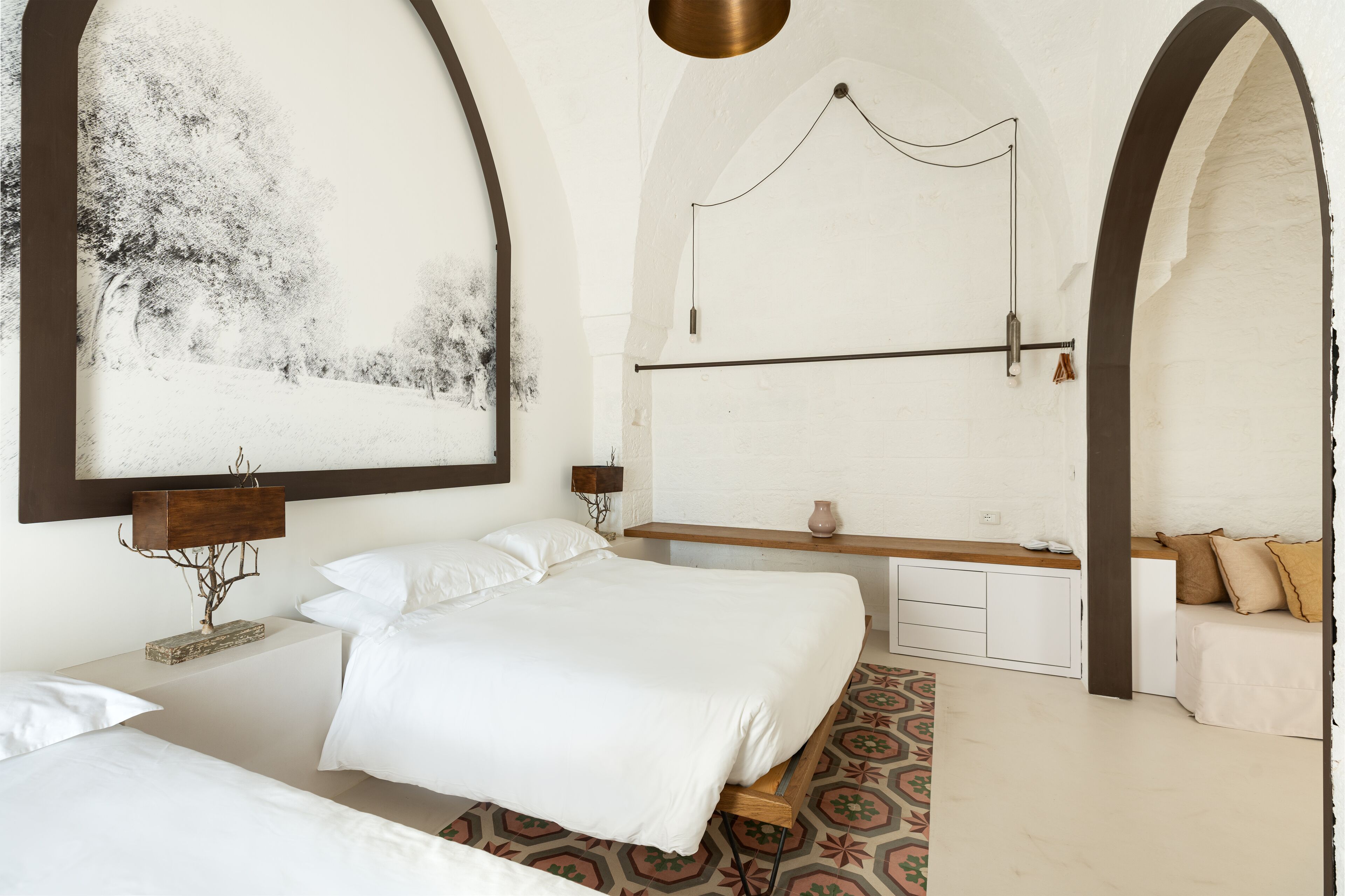 A bedroom with two beds, a wooden bench, a hanging light fixture, and a large abstract painting.