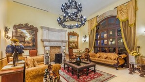 A spacious living room with a fireplace, a chandelier, and a large window with curtains. - Experience the Ultimate in Comfort & Convenience: 1BR Condo in Hacienda Encantada (Cabo San Lucas)