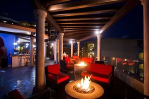 An outdoor patio area with red seating, a fire pit, and a covered section with columns and a bar. - Hacienda Encantada 2BR Condo with Tennis Court (Cabo San Lucas)