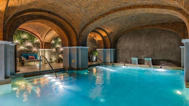 Una piscina interior con techos de ladrillo en arco y una zona de estar con asientos y plantas.