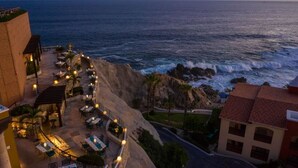 Un hôtel situé sur la côte, doté d’une terrasse avec vue sur l’océan, d’un escalier menant à l’étage supérieur et d’un bâtiment surmonté d’un toit recouvert de tuiles rouges.