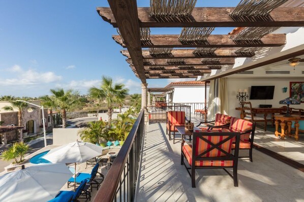 A balcony with outdoor seating, a pool, and a view of palm trees and buildings. - Experience the Ultimate in Comfort & Convenience: 3BR Condo with Pool (Cabo San Lucas)