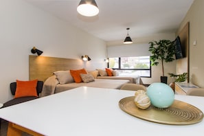 Une chambre d’hôtel moderne, dotée d’un canapé, d’une table à manger et d’une grande fenêtre donnant sur les bâtiments environnants.