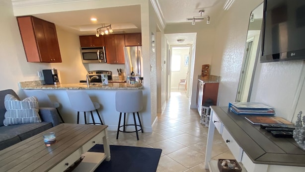 A modern kitchen with a central island, a dining area with a table and chairs, and a TV mounted on the wall. - Westwinds Waterfront Luxury Condo Beach and Pool (Treasure Island)